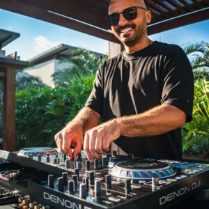 Bald DJ smiling while mixing tracks at Pipa Beach, Brazil.