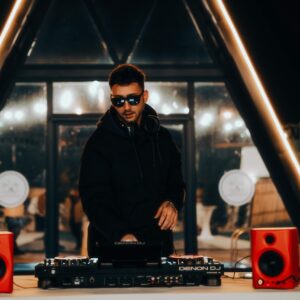 DJ mixing at night, surrounded by vibrant lights and audio equipment in a stylish venue.